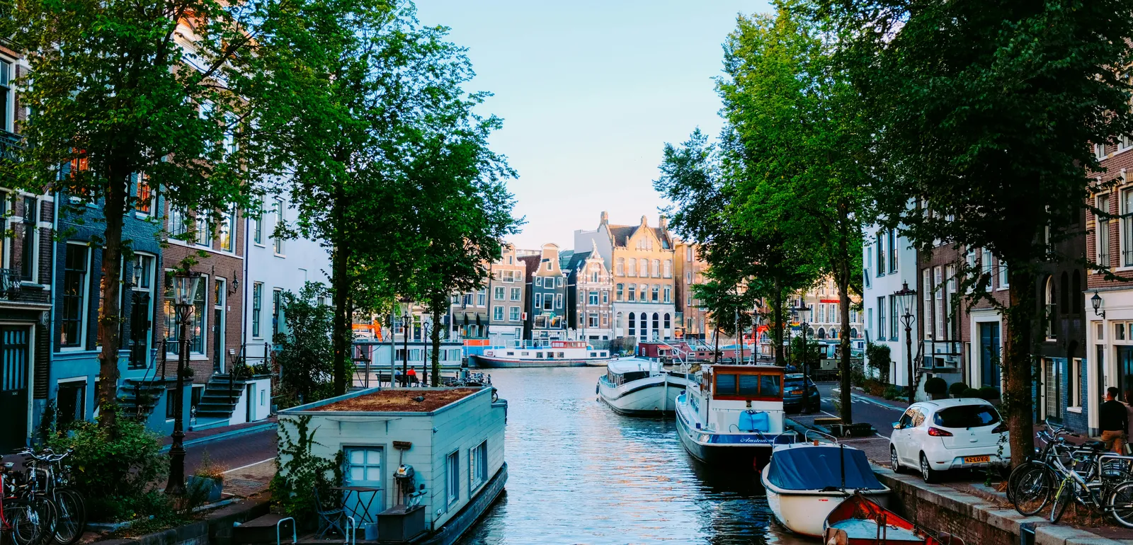 Peaceful scenery of Amsterdam streets with typical houses against channel with moored boats on clear sunny day